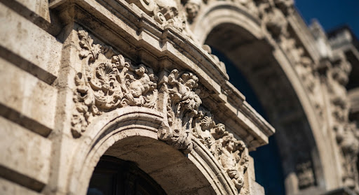 Classical stone carving on a historic building facade, in sharp sunlight and shadow.